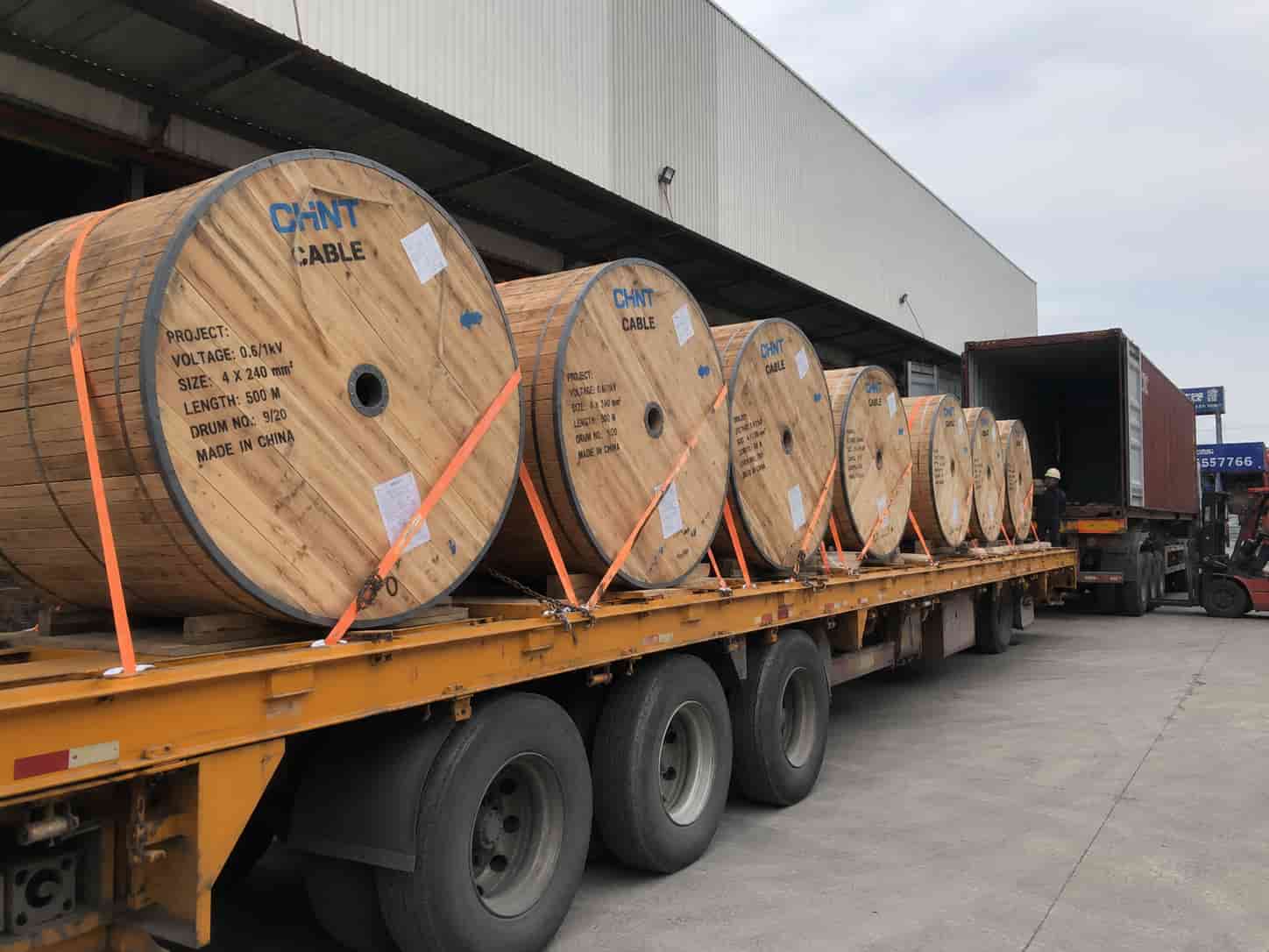 Large wooden cable drums loaded on a flatbed truck at an industrial loading bay, ready for international shipment to a utility power project.