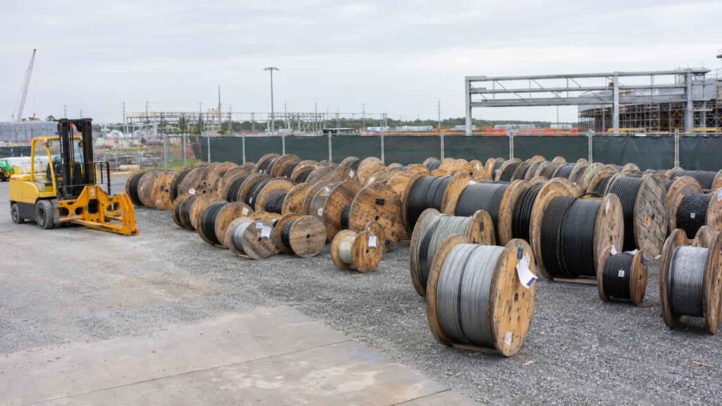 Large cable drums stored upright in a project site laydown area with forklift handling equipment and organized drum register