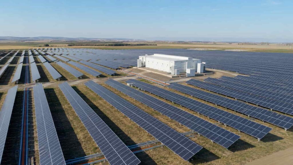 Aerial view of a large ground-mounted solar farm with cable trays and inverter stations visible between panel rows